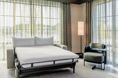 a bed and a chair in a room with windows at AC Hotel by Marriott Saratoga Springs in Saratoga Springs