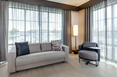 a living room with a couch and a chair and large windows at AC Hotel by Marriott Saratoga Springs in Saratoga Springs