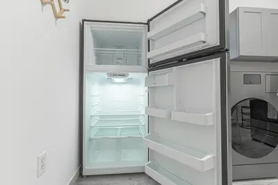 an empty refrigerator with its door open in a kitchen at Modern Comfort 2BR with Washer & Dryer Near Subway & LGA in Corona