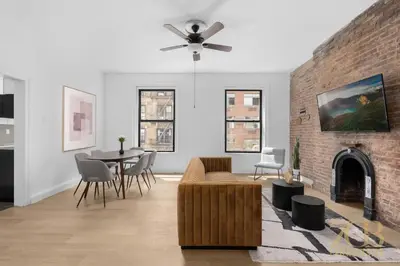 a living room with a ceiling fan and a brick fireplace at State-of-the-Art Loft-Style 2Br Apartment - Laundry - Chelsea in New York
