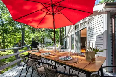 a wooden table with a red umbrella on a porch at Riverfront Retreat Hot Tub, Firepit & Pool Table in Cuddebackville