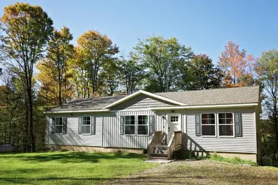 a small white house with trees in the background at Oneonta Hideaway in Oneonta
