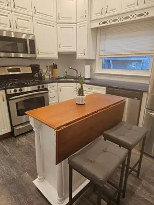 a kitchen with white cabinets and a kitchen island with stools at Cozy Getaway 3-Prudential Center, NJPAC, Penn Station in Kearny