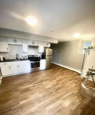 a kitchen with white cabinets and a wooden floor at Brand New House in Bronx