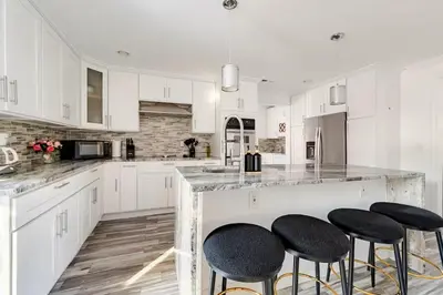 a white kitchen with white cabinets and black stools at Norwalk Retreat in Norwalk