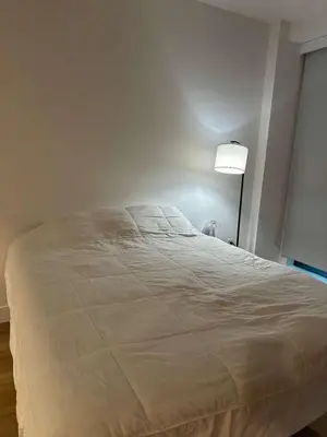 a white bed in a bedroom with a lamp at Bright, Modern Studio in White Plans in White Plains