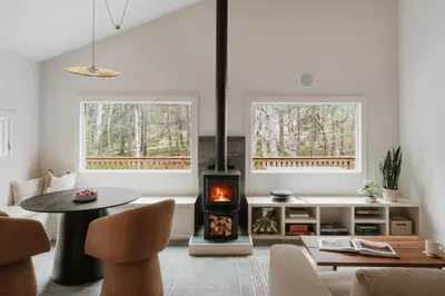 a living room with a wood stove and two windows at Creekside Modern Cabin Sauna Hot Tub Niksen Den in Callicoon