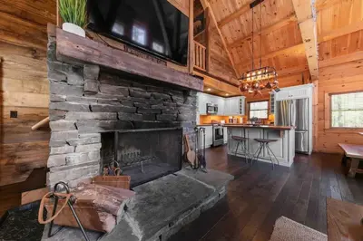 a living room with a stone fireplace in a cabin at Cozy Log Cabin with Hot Tub 10 Min to Hunter Mtn in Jewett