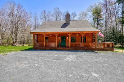 a log cabin with a porch and an american flag at Cozy Log Cabin with Hot Tub 10 Min to Hunter Mtn in Jewett