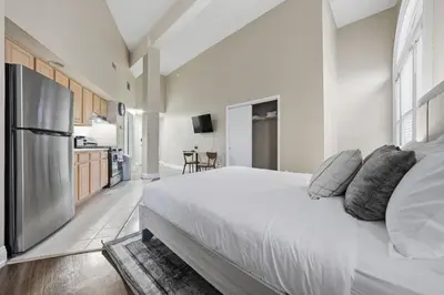 a white bedroom with a large bed and a kitchen at Relaxing studio perfect for extended visits in New Haven