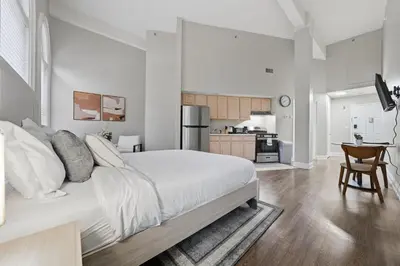 a white bedroom with a large bed and a kitchen at Relaxing studio perfect for extended visits in New Haven