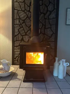 a wood stove with a fire in a room at Little Longbow Lakefront Chalet in Becket