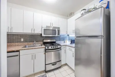 a kitchen with white cabinets and a stainless steel refrigerator at Chelsea 1BR in Shared Apt with Laundry and Rooftop in New York