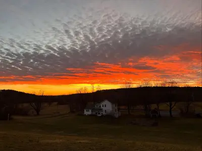a cloudy sky with a house in a field at sunset at Gorgeous Hudson Valley Farmhouse on 14 Acres home in Old Chatham