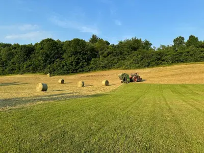 a tractor in a field with hay bales at Gorgeous Hudson Valley Farmhouse on 14 Acres home in Old Chatham