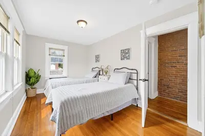 two beds in a white room with a brick wall at 14 Guest, 9 Bed, Family Getaway- 30 min from NYC in New Rochelle