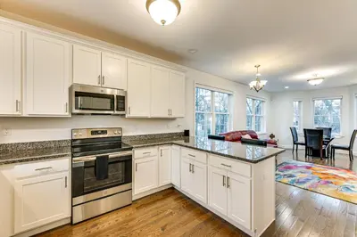 a kitchen with white cabinets and appliances and a living room at 2 Mi to The Mark Twain House and Museum Airy Escape in West Hartford