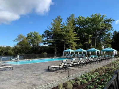 a swimming pool with chairs and blue umbrellas at Landing Apartments - The Preserve at Great Pond in Windsor