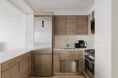 a kitchen with wooden cabinets and a stainless steel refrigerator at Blueground Midtown East fitness center nr UN NYC-2172 in New York