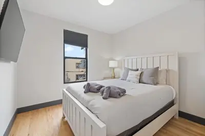a white bedroom with a large white bed with a window at New Luxury and Chic 3BR 2BA Apartment 20 Minutes to NYC in Jersey City