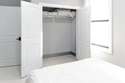 a white bedroom with a bed and two open doors at 20 Minutes to Times Square with Free Indoor Parking in West New York
