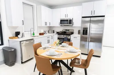 a white kitchen with a wooden table and chairs at Easy Access to Times Square and Metlife Stadium Free Parking in West New York