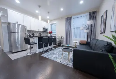 a living room with a black couch and a kitchen at Brand New 3BR 2BA next to Central Park, elevator in New York