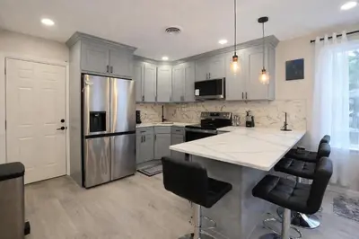 a kitchen with white cabinets and a large island with black chairs at Bright Renovated 3BR Apartment w Private Entrance