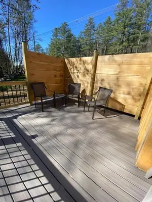 three chairs on a deck with a wooden fence at Cozy stream-side cabin in Lanesborough