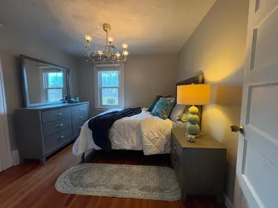 a bedroom with a bed and a dresser and a lamp at Cozy Apartment in Watertown
