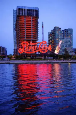 a large neon cola sign in front of a city at Room in a 2 Bedrooms Apartament Long Island City, Kitchen and Bathroom shared with very nice host in New York