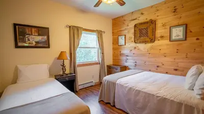 two beds in a bedroom with wooden walls and a window at Mins to Hunter Mountain • Sleeps 36 • Pool Spa Games Bar Cozy Peaks Lodge by AvantStay in Tannersville