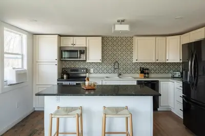 a kitchen with white cabinets and a black refrigerator at Rustic Luxe Creekside Retreat with Hot Tub and Fire Pit, Minutes From Hudson in Hudson
