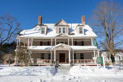 a large white house with snow on it at The Berkshire Mountain Inn in Great Barrington