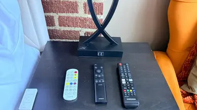 three remote controls sitting on a table next to a lamp at 2-Joint Large Deluxe Rooms in Private House - NYC in Sunnyside