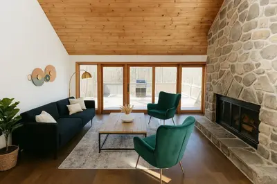 a living room with a stone fireplace and green chairs at Drift Haus 4 and half BR Mountain Lodge in Windham