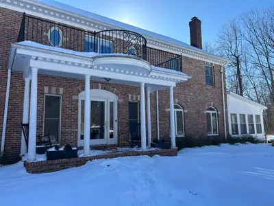a red brick house with a white porch in the snow at Luxury Private Estate, 5BR 6BA, close to MetLife with ample parking in Green Village