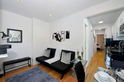 a living room with a black couch and a kitchen at Cityscape 2 Bedroom Unit Prime Location in New York
