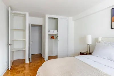 a white bedroom with a white bed and a closet at Blueground Yorkville pool nr Central Park NYC-2218 in New York