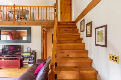 a wooden staircase in a living room with a couch at Log Cabin at the Goat Sanctuary in Napanoch