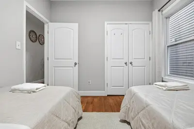 a white bedroom with two beds and a window at Sleeps 19 • 15ft Celings • Near NYC in Jersey City