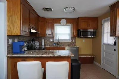 a kitchen with wooden cabinets and white stools at Pet Friendly 3BR New Britain Home with King Bed Near Hartford Sleeps 8 in New Britain