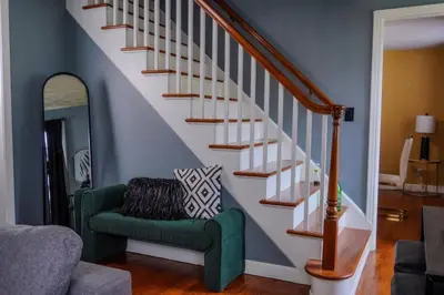 a living room with a staircase with a green chair at Pet Friendly 3BR New Britain Home with King Bed Near Hartford Sleeps 8 in New Britain