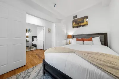 a bedroom with a large bed with white walls and wooden floors at Fast access to NYC - family & group -skyline view in Jersey City