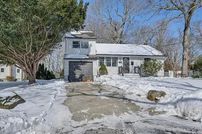 a white house with snow on the driveway at Easy Transit to NYC! Sleek North Shore Hideaway in Huntington Station