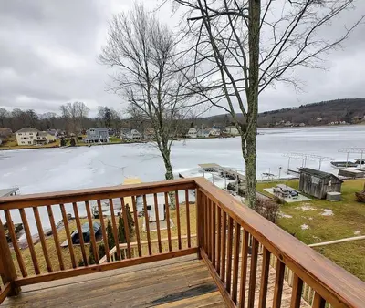 a wooden deck with a view of a frozen lake at Waterfront Cottage at Highland Lake with Dock in Winsted