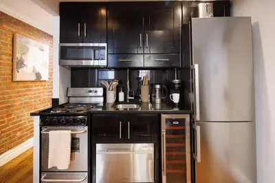 a kitchen with black cabinets and a stainless steel refrigerator at Urban Oasis 1BR East Village Hideaway with Patio! in New York