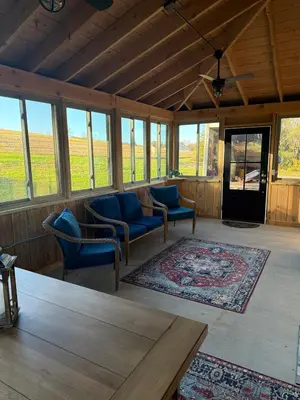 a living room with chairs and a table and windows at Cattail Cabin in Waterville
