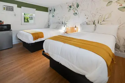 two beds in a hotel room with white sheets and yellow blanket at Birches Motel in Saratoga Springs