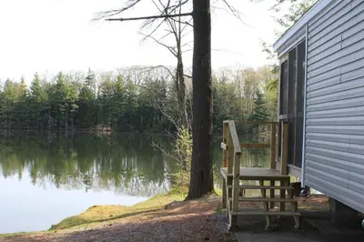 a chair sitting on the side of a house next to a lake at Alpine Lake Lakefront Park Model 4 in South Corinth